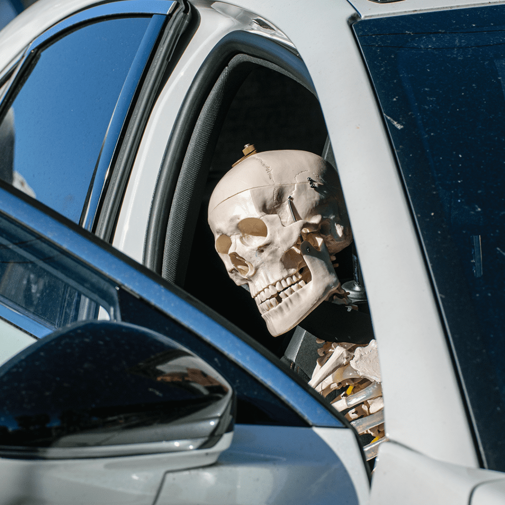 A Halloween skeleton sitting in the passenger seat of a car